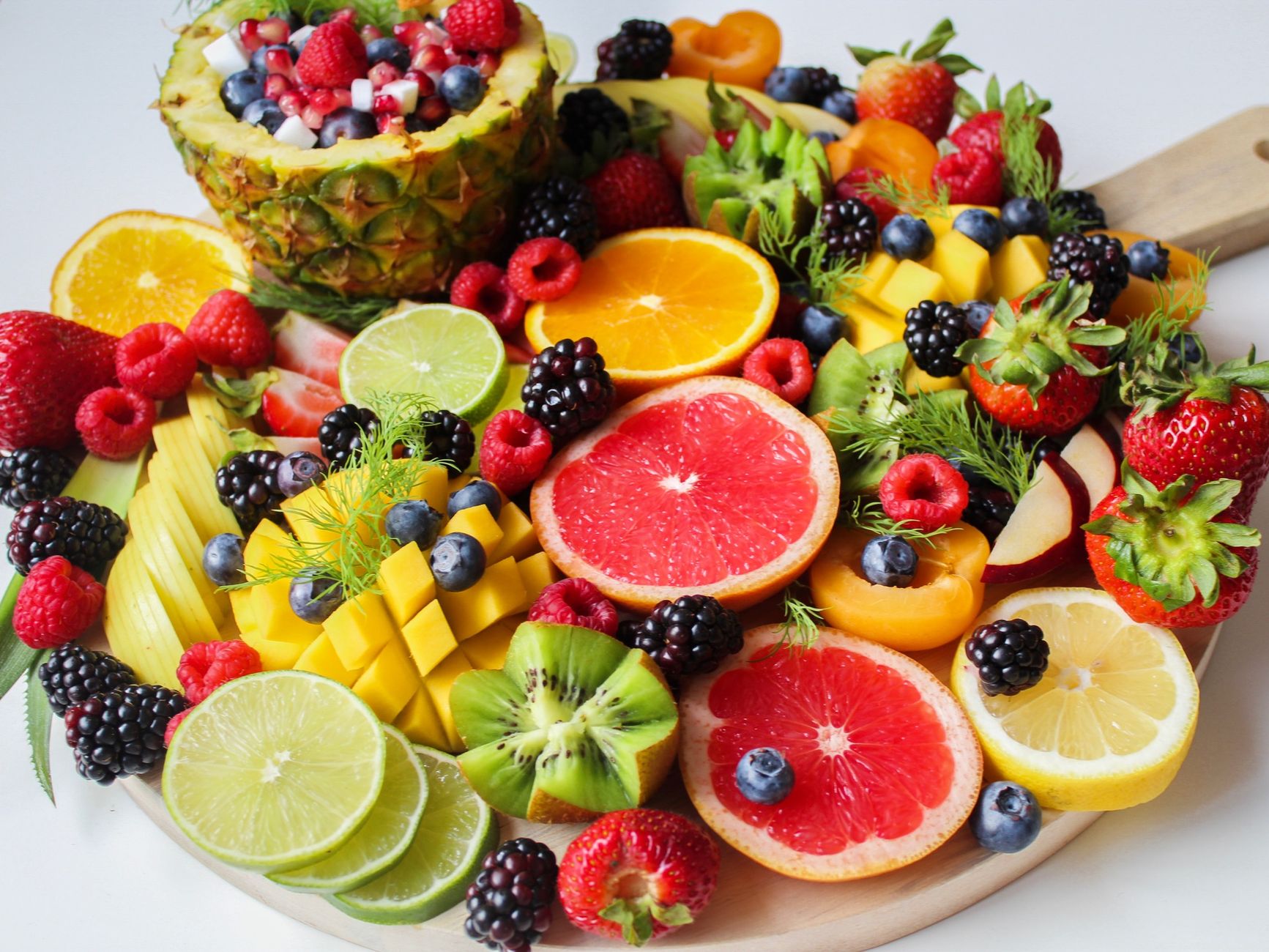 A platter of sliced fruit and berries including pineapple, strawberries, citrus, and kiwi