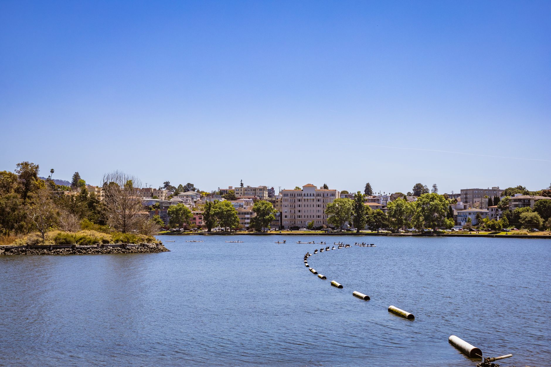 A calm blue lake with buildings and trees along the far shore under a clear sky