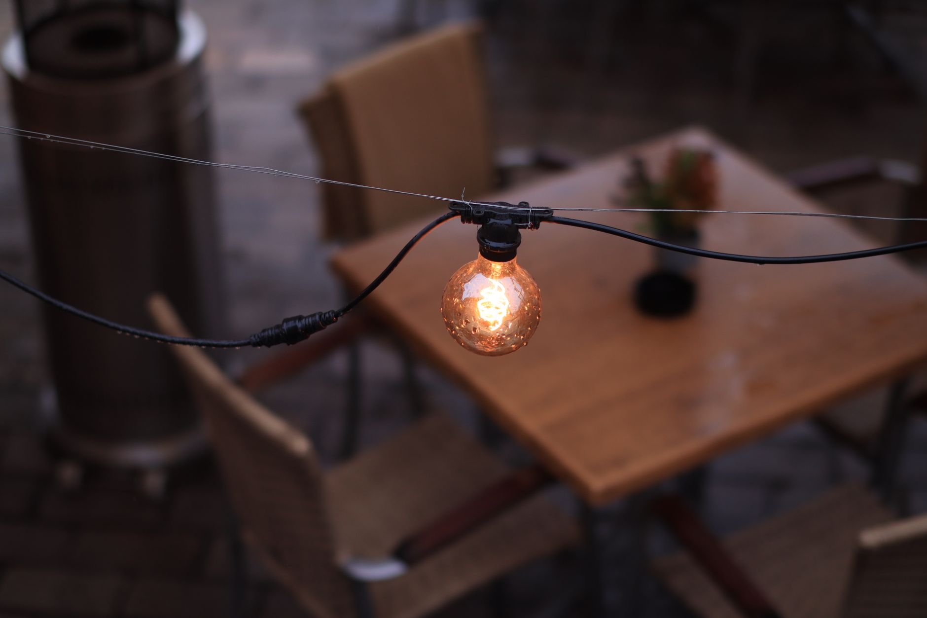 A glowing string-light bulb over a wooden table on a dim outdoor patio