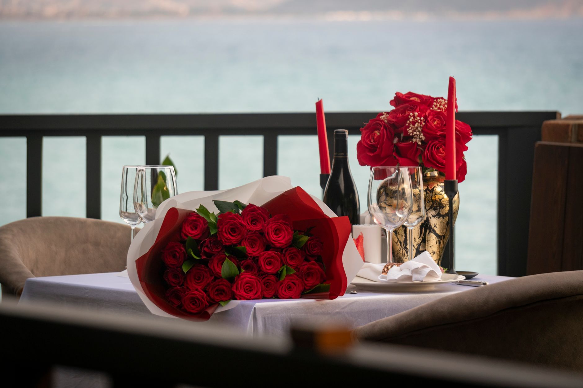 A balcony dinner table with red roses, a bottle of wine, glasses, and red candles