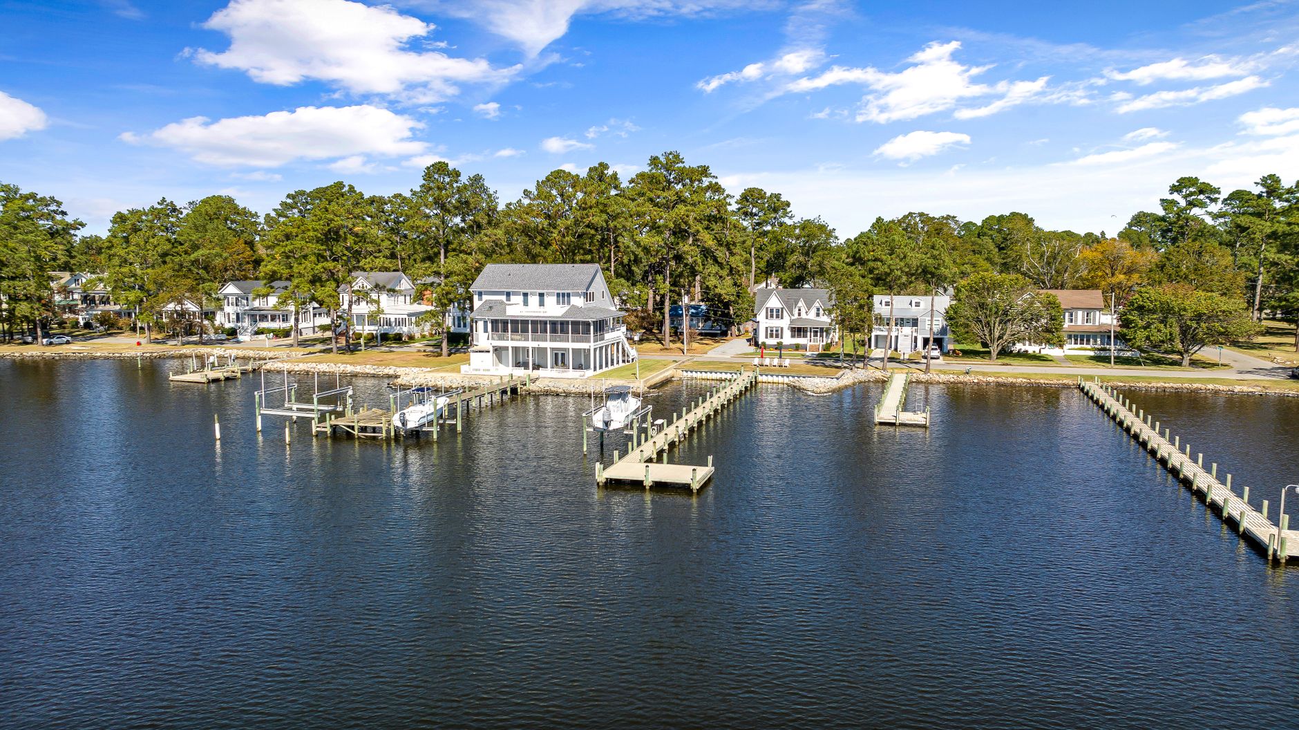 An aerial view of waterfront homes with docks along a calm bay lined with tall trees