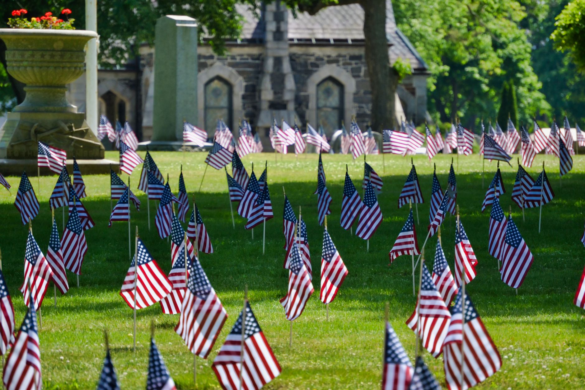Rows of small American flags standing on a green lawn in front of a stone chapel
