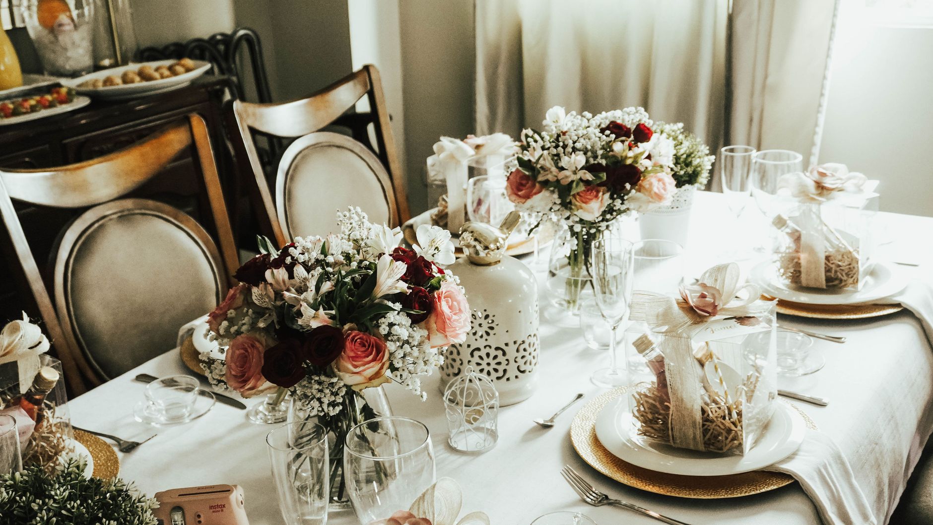 A dining table with bouquets of roses and baby&rsquo;s breath, wrapped gift boxes, and glasses