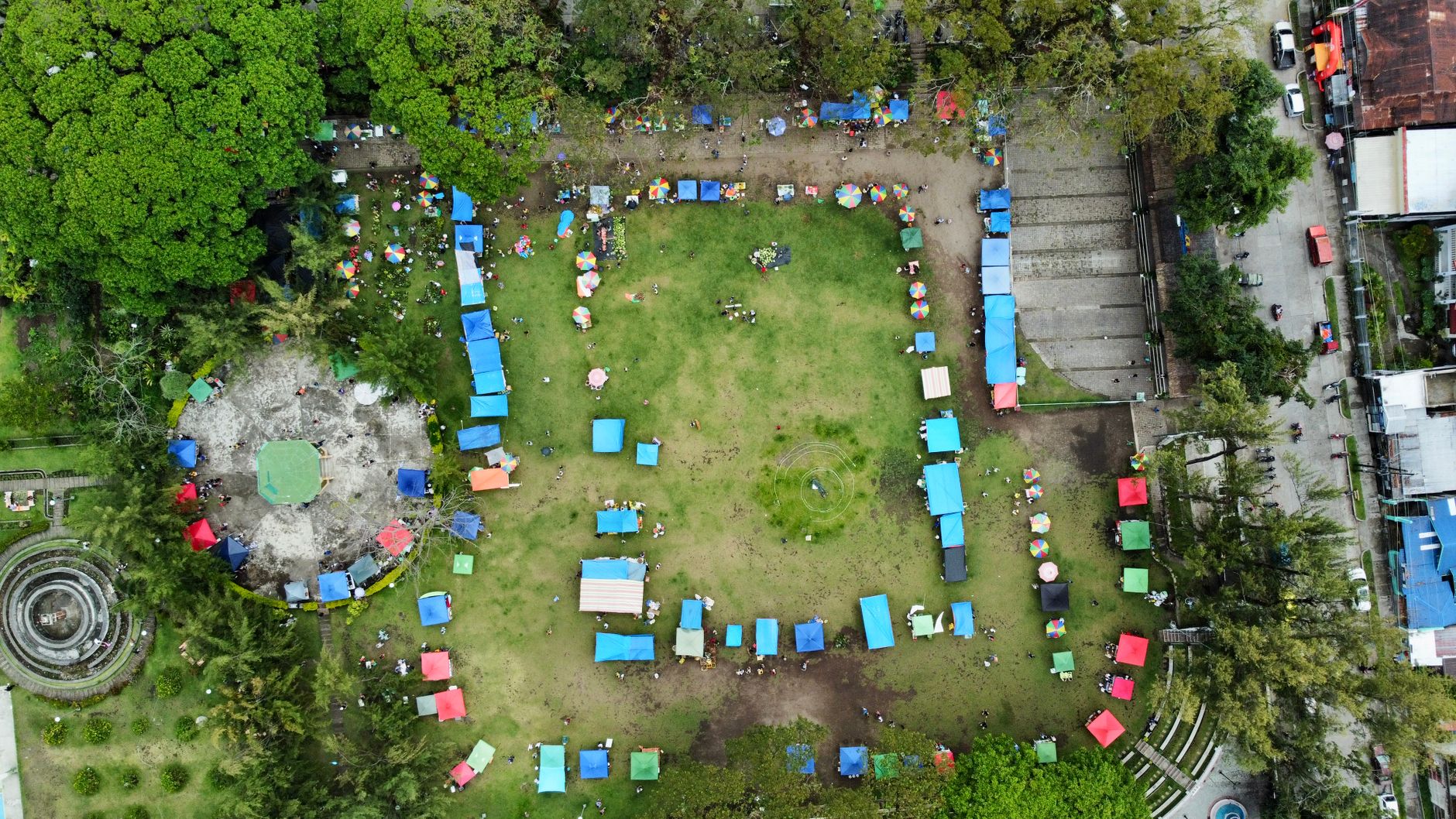 An aerial view of a lively outdoor market with colorful tents set up around a green lawn