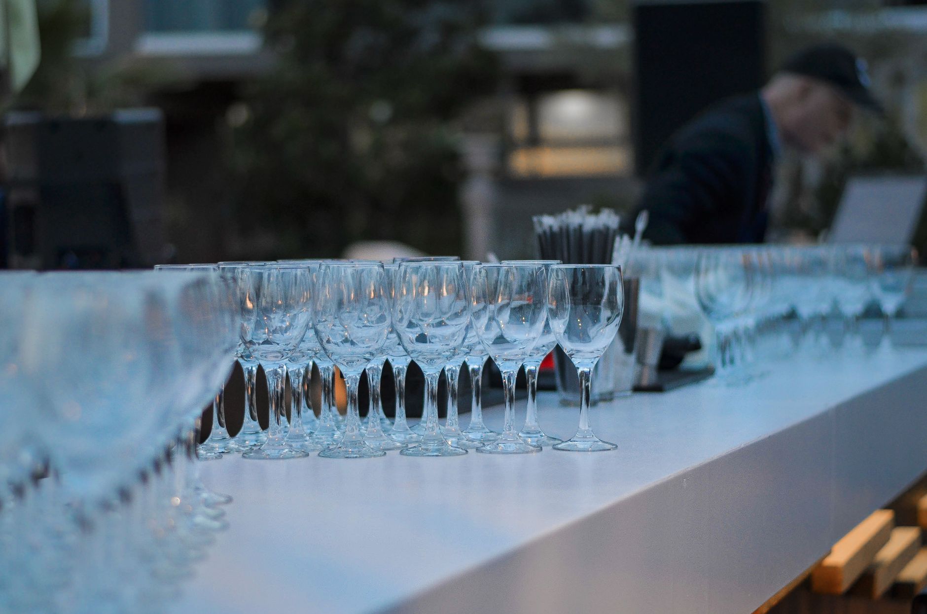 A long white bar table lined with empty wine glasses in the evening