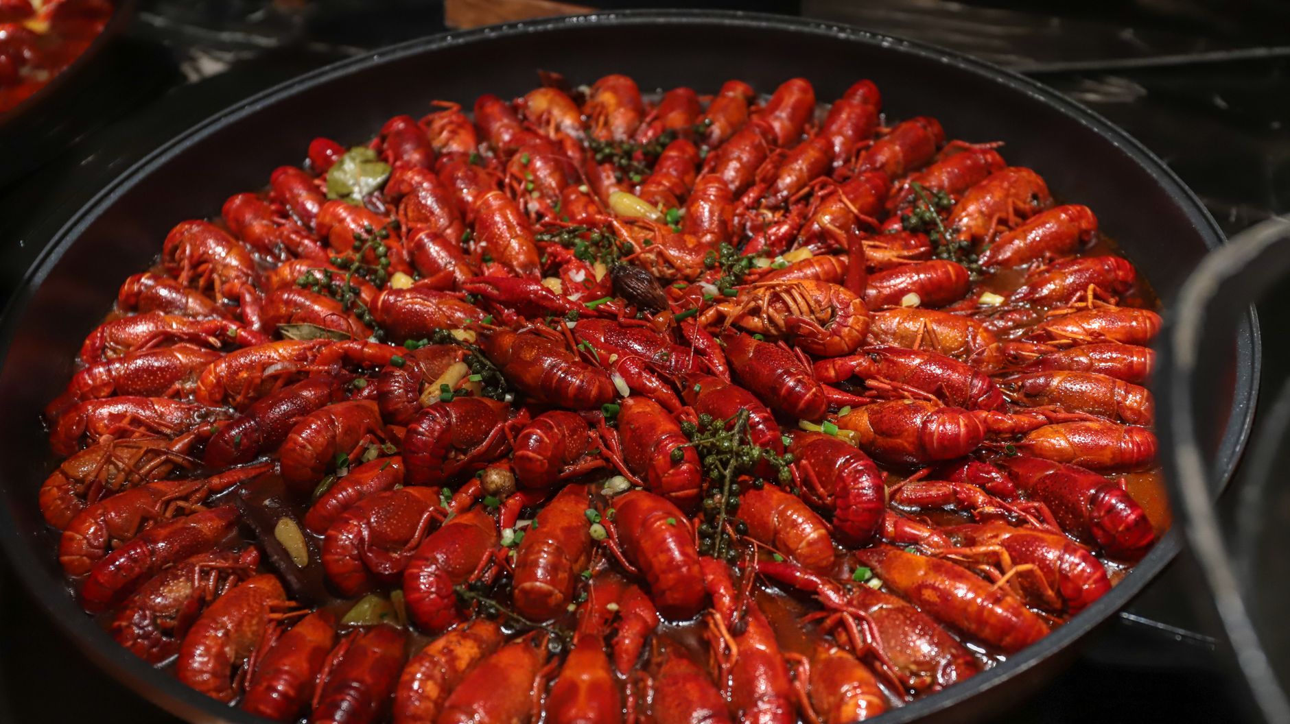 A large pan of spicy red crawfish garnished with herbs