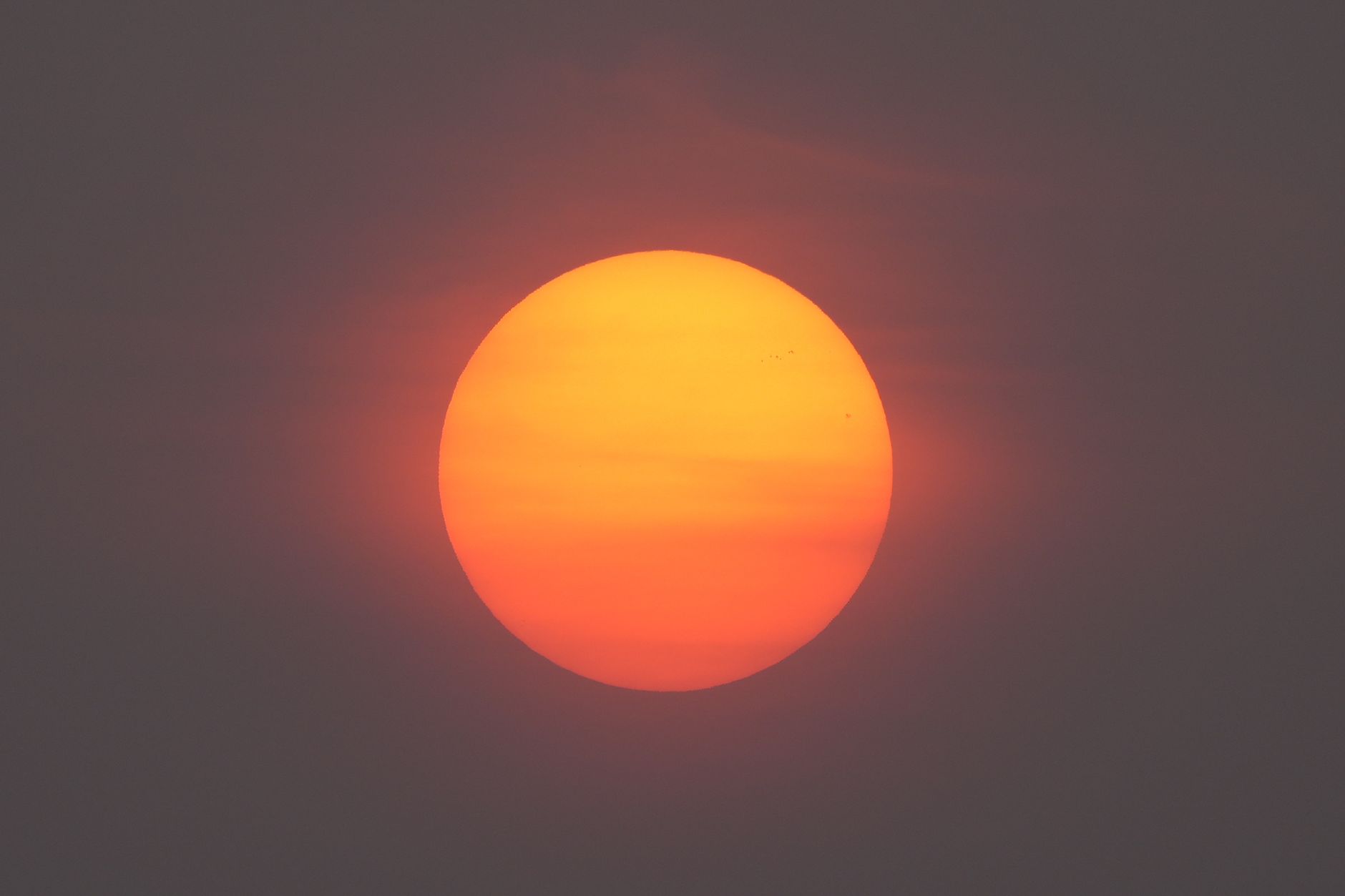 A deep orange sun glowing through a gray wildfire haze