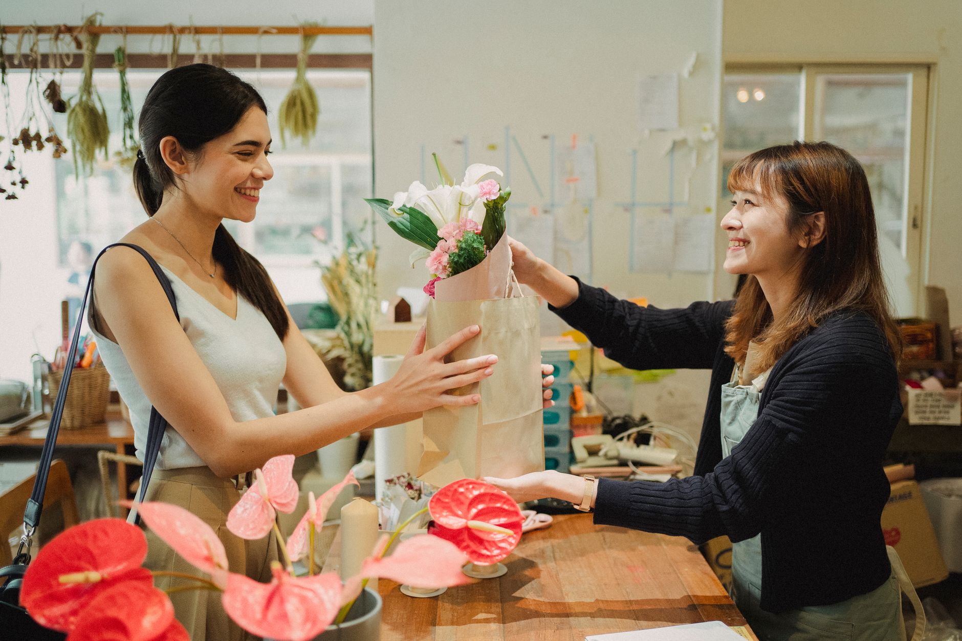 Una florista sonriente entregando un ramo de flores envuelto a una clienta en el mostrador de la tienda