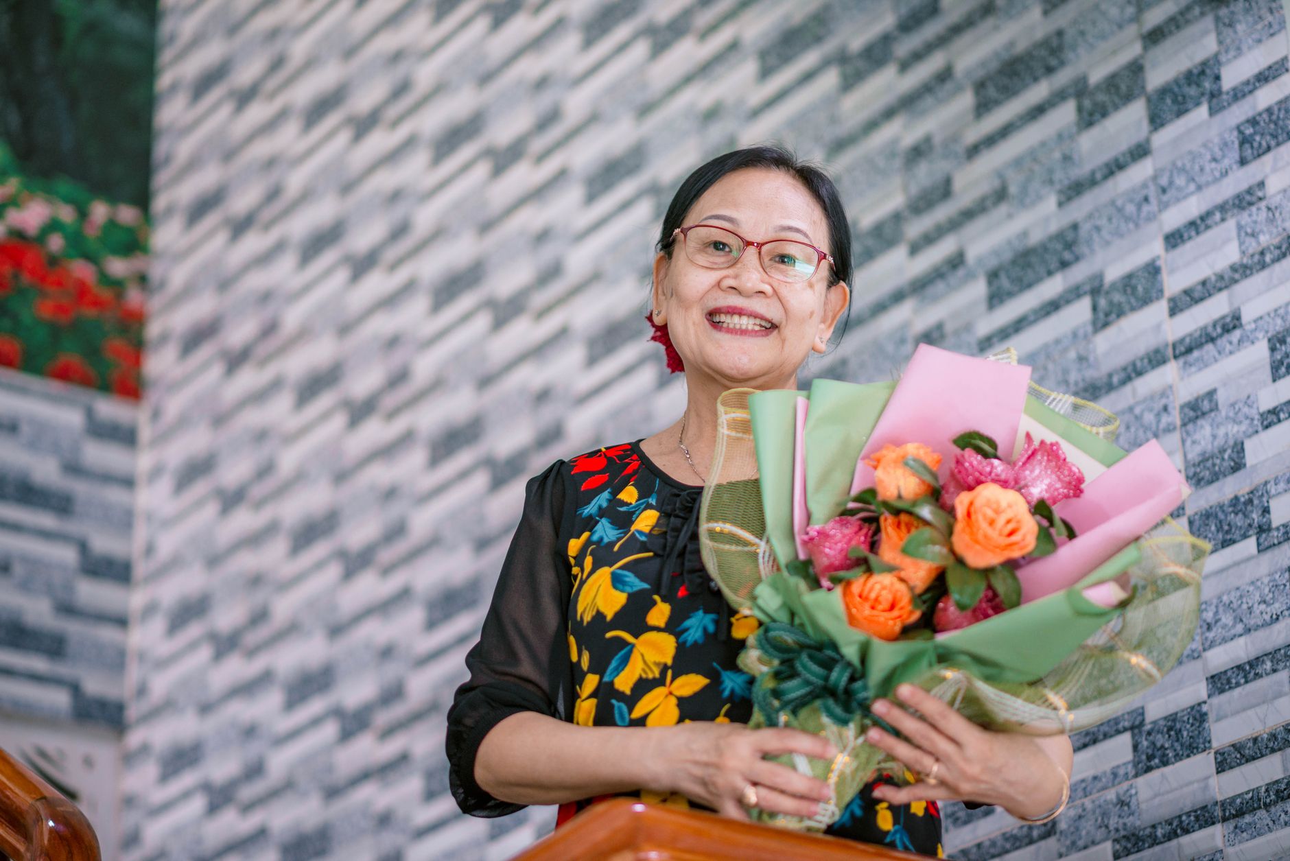 A smiling senior woman holding a vibrant, colorful flower bouquet outdoors