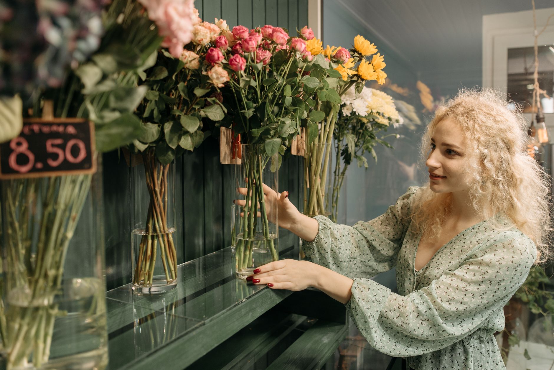 A woman comparing bouquets of roses and sunflowers next to a visible price tag in a flower shop