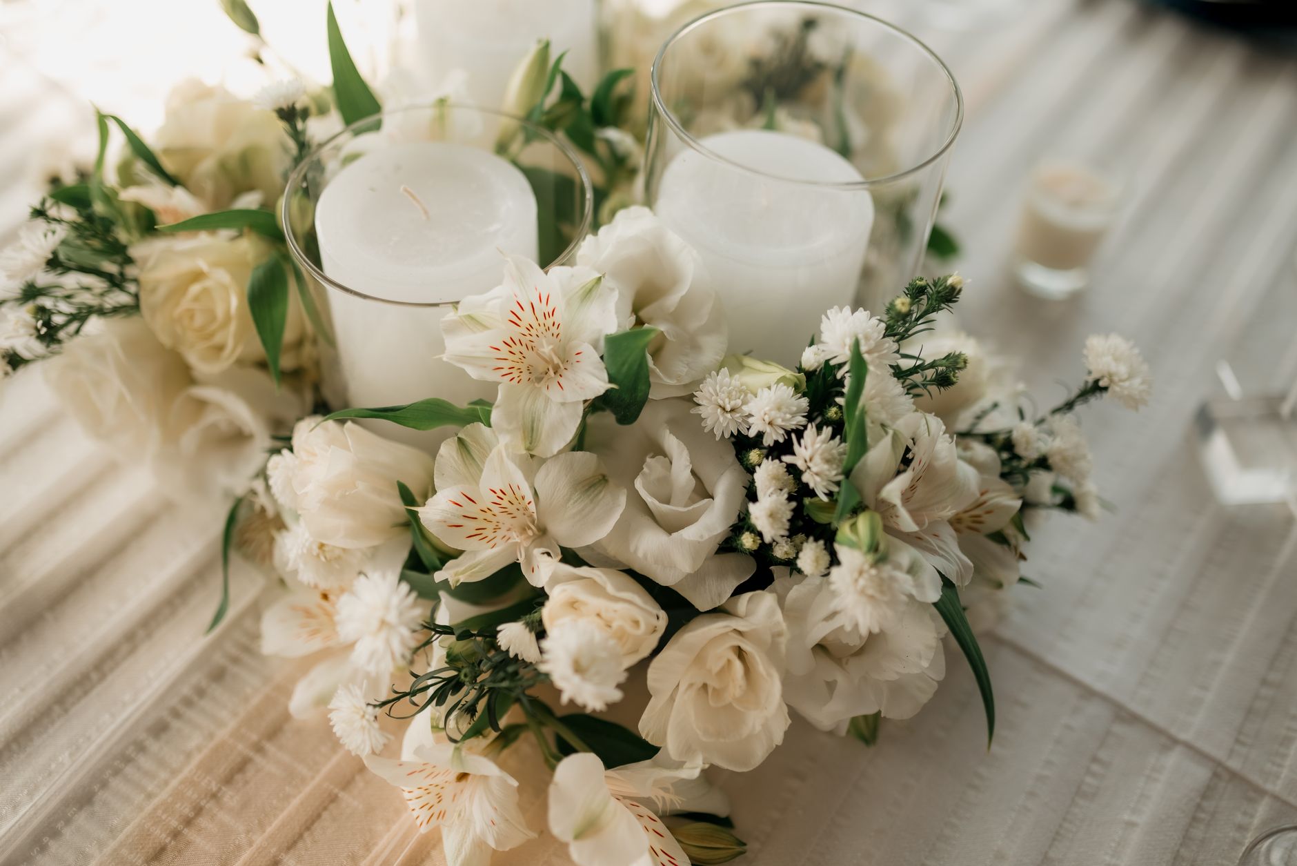 A low arrangement of white roses and alstroemeria around two glass-enclosed candles