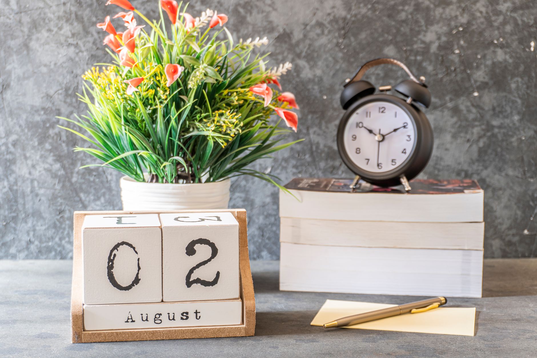 A wooden block calendar, an alarm clock, a notepad, and a potted plant with orange flowers